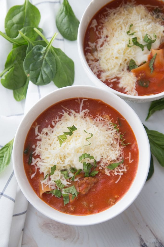 Two bowls of healthy gluten free instant pot soup sitting on a white backdrop next to basil leaves and spinach