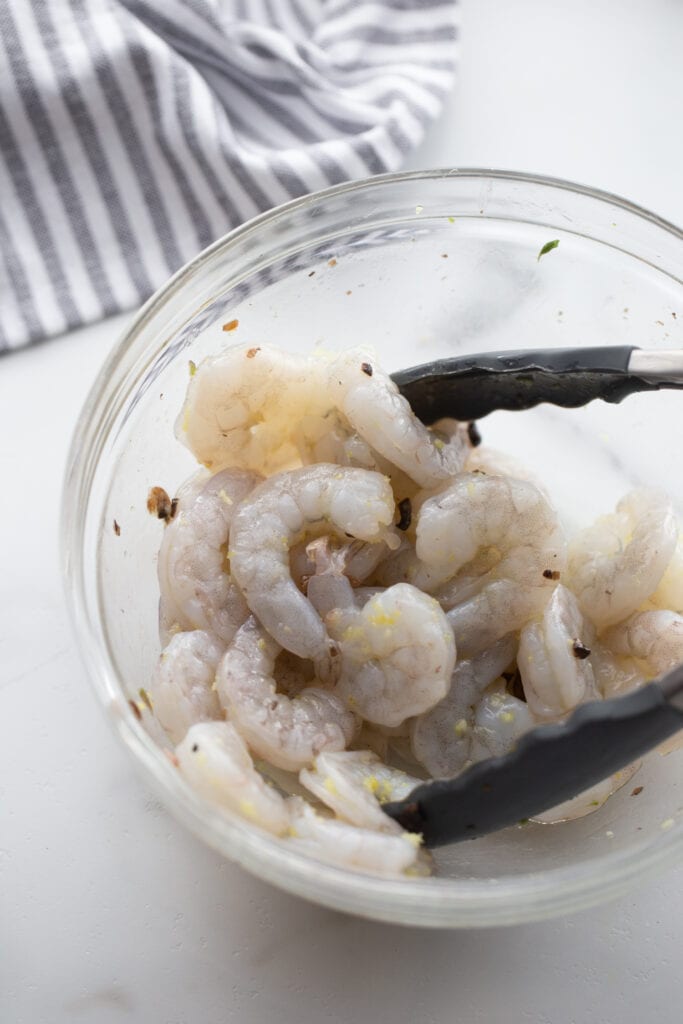 Raw shrimp are being mixed in a glass bowl.