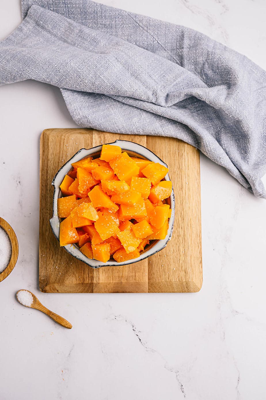 Overhead photo: of cubed butternut squash in a bowl on a wooden trivet.