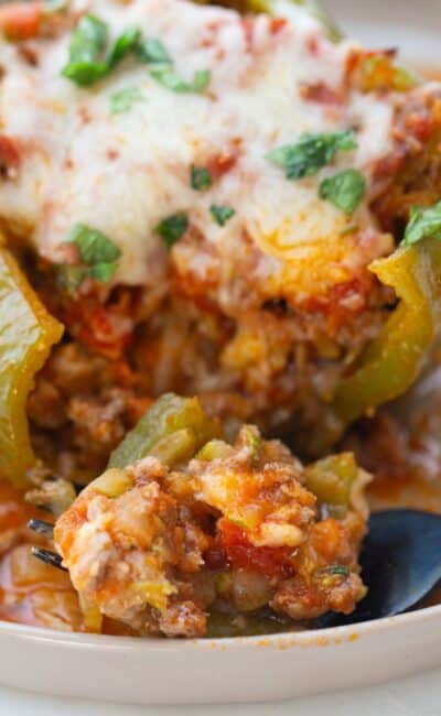 An Italian Stuffed Green Bell Pepper topped with cheese with a fork full of a bite of filling on a white rimmed plate.