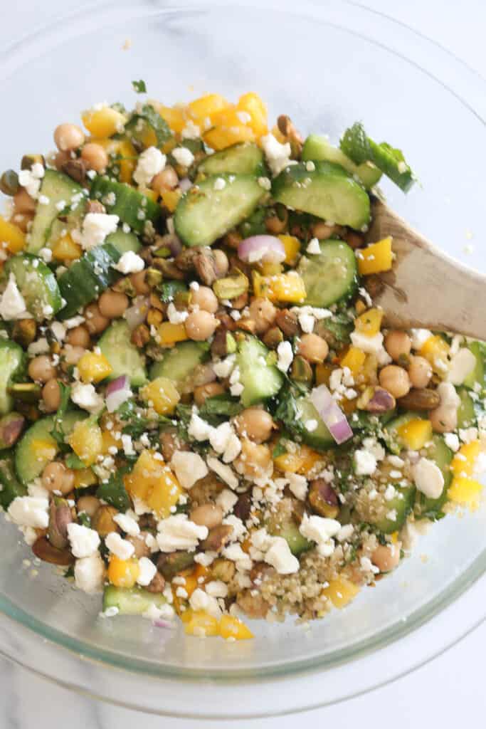 Mixing bowl with chickpeas, quinoa, fresh veggies, and feta cheese.