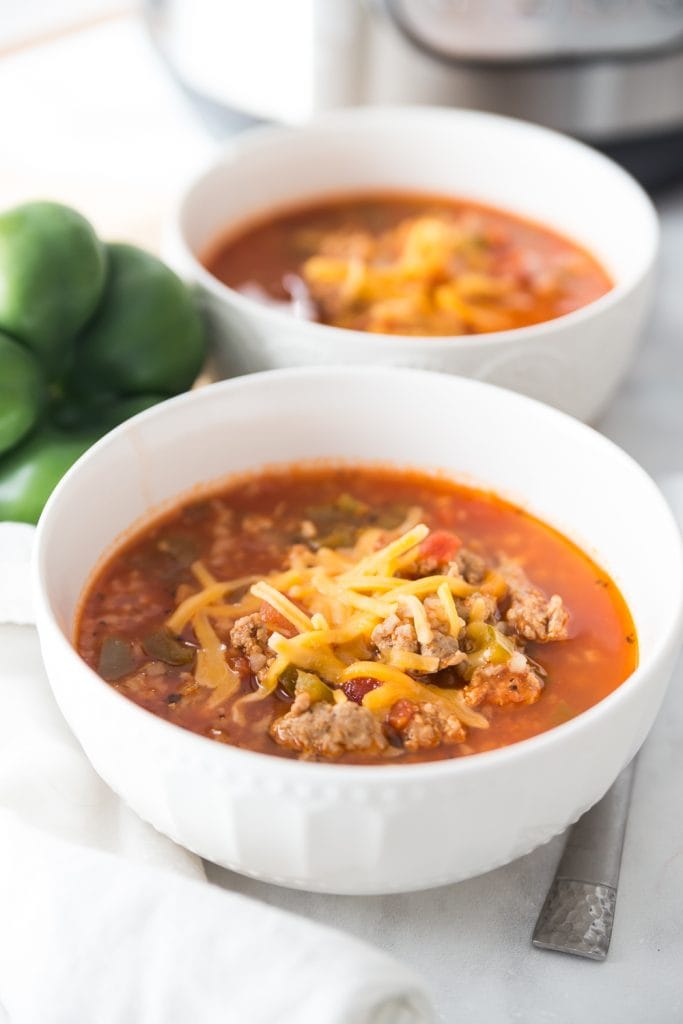 Two small white bowls with low carb stuffed pepper soup in front of an Instant Pot on white fabric napkins. 