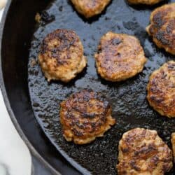 A cast iron skillet with homemade chicken sausage patties cooked golden brown.