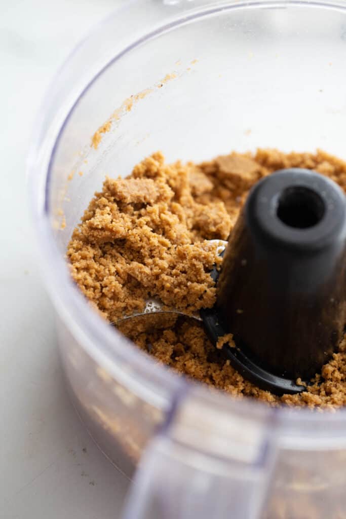 High angle photo of crushed graham crackers and melted butter in a food processor, to be used as crust.