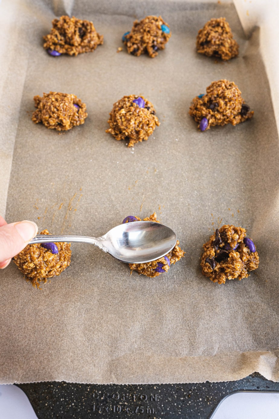 A spoon is pressing down on a monster cookie dough ball.