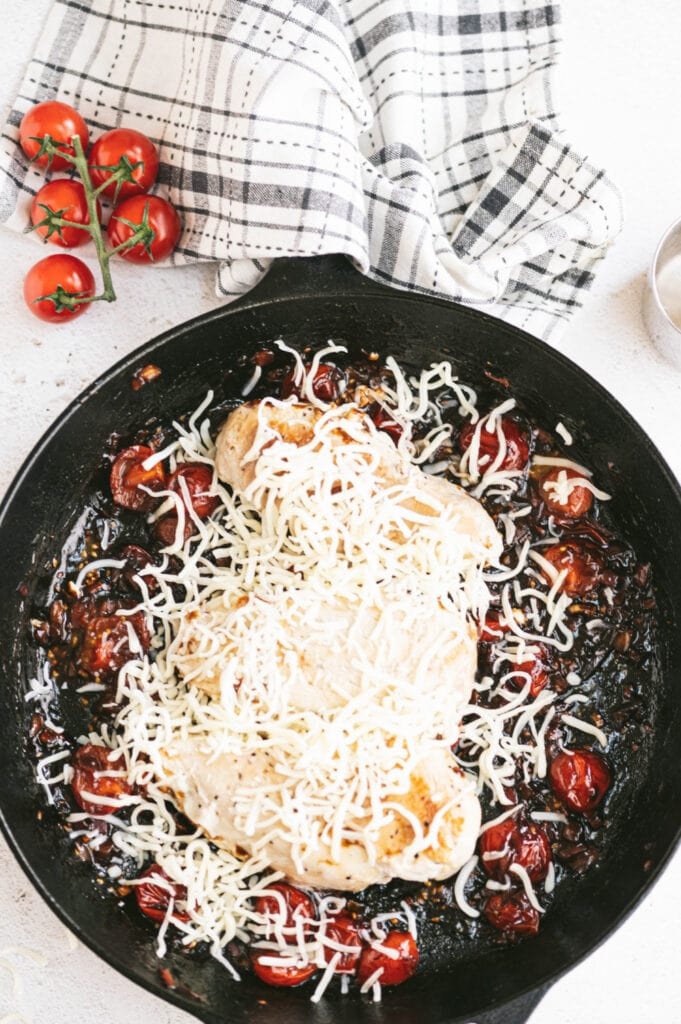 Overhead photo of a cast iron skillet full of caprese chicken, in process. The mozzarella cheese needs to melt on top of the chicken and tomato mixture.