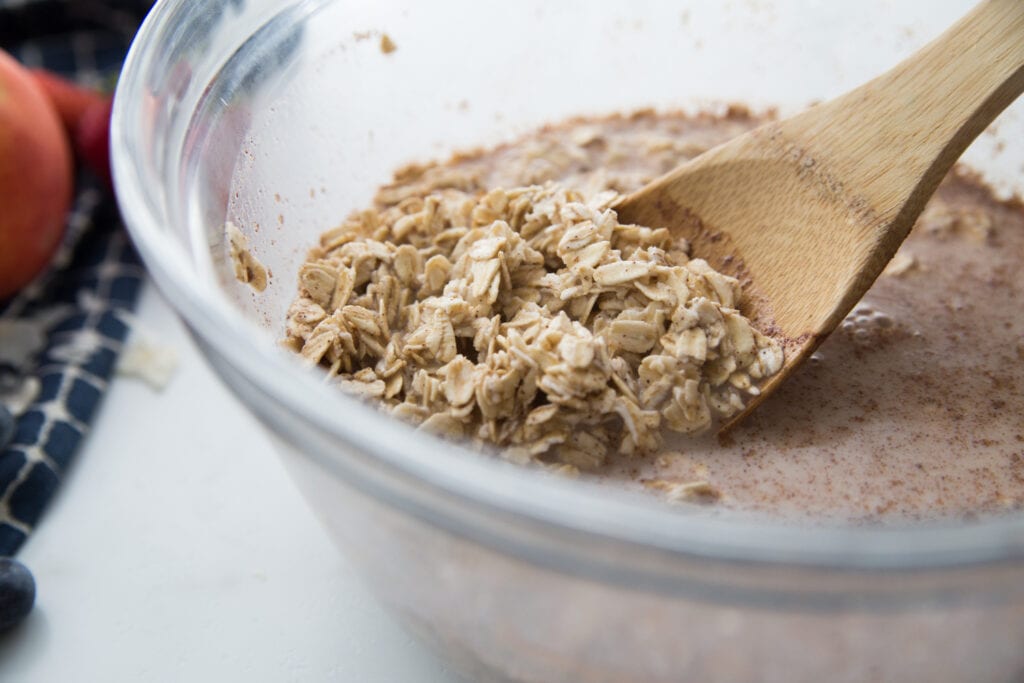 A bowl of oats, almond milk, and cinnamon with a wooden spoon