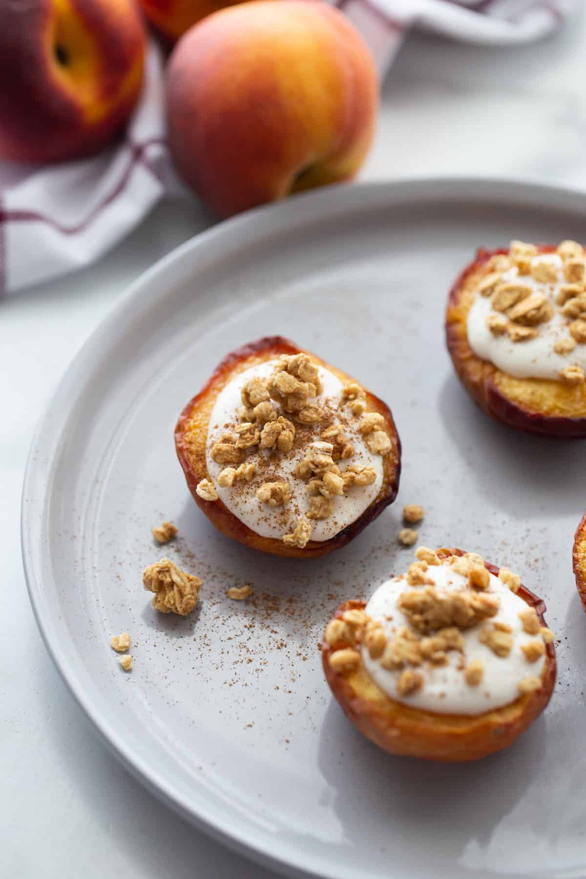 Three air fried peach halves on a white plate topped with whipped ricotta cinnamon and granola