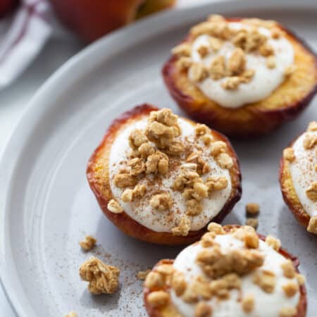 Three air fried peach halves on a white plate topped with whipped ricotta cinnamon and granola