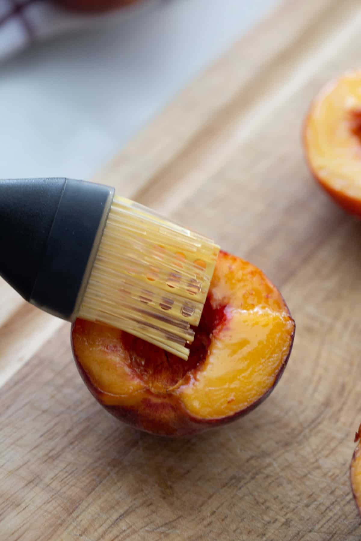 Half of a peach with coconut oil being brushed on top