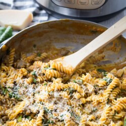 large saucepan with pumpkin pasta and spicy sausage topped with shredded parmesan cheese. pan is resting on a blue and white checkered napkin. Instant Pot is in the background of the photo