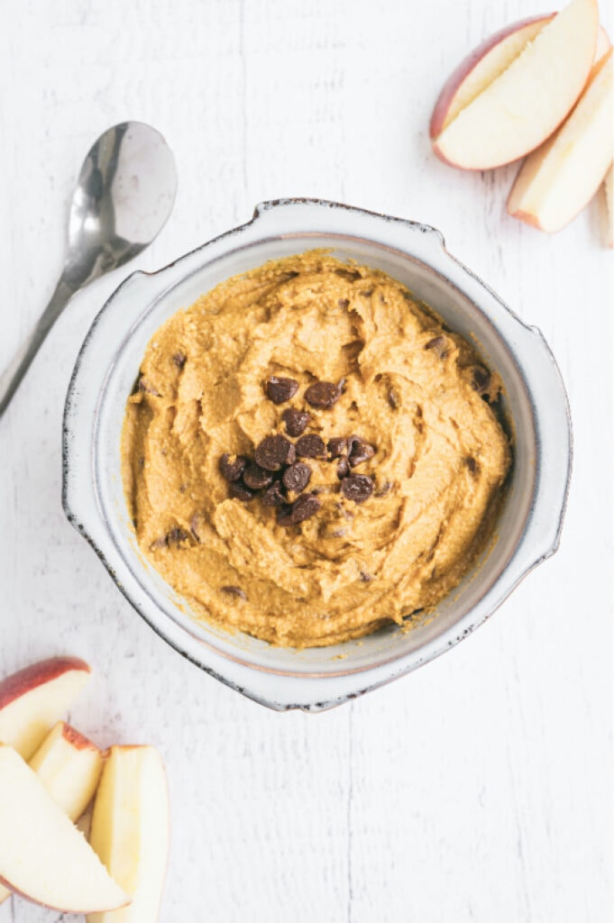 overhead image: bowl of vegan dessert dip topped with dairy free chocolate chips, surrounded by red apple slices