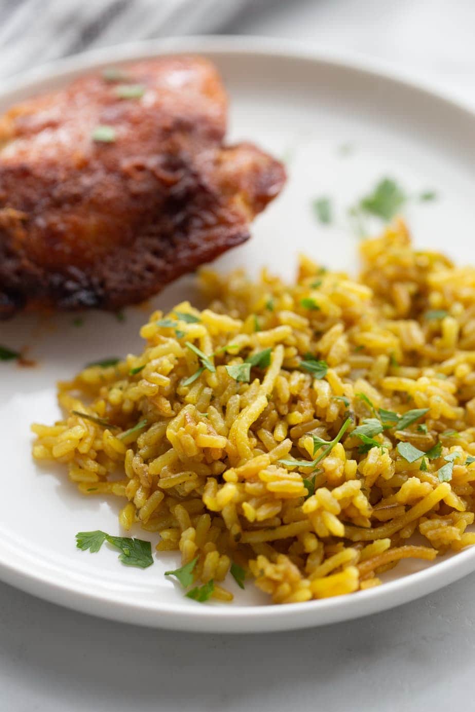 A close up of Instant Pot Rice a Roni on a white plate with spiced rubbed chicken slightly out of focus in the background