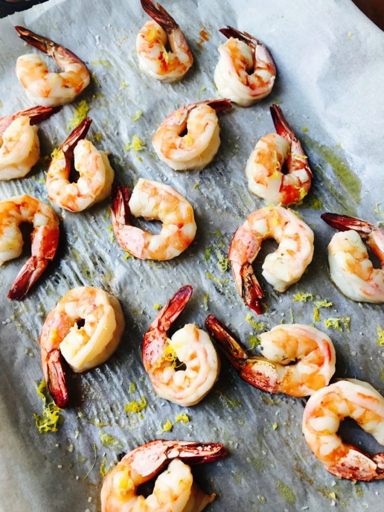 Roasted shrimp on a parchment lined sheet pan with lemon zest garnish