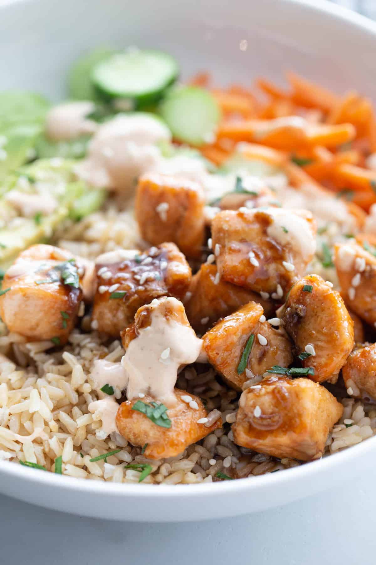 Bowl of sticky air fryer salmon bites over brown rice with spicy mayo sesame seeds and cilantro.