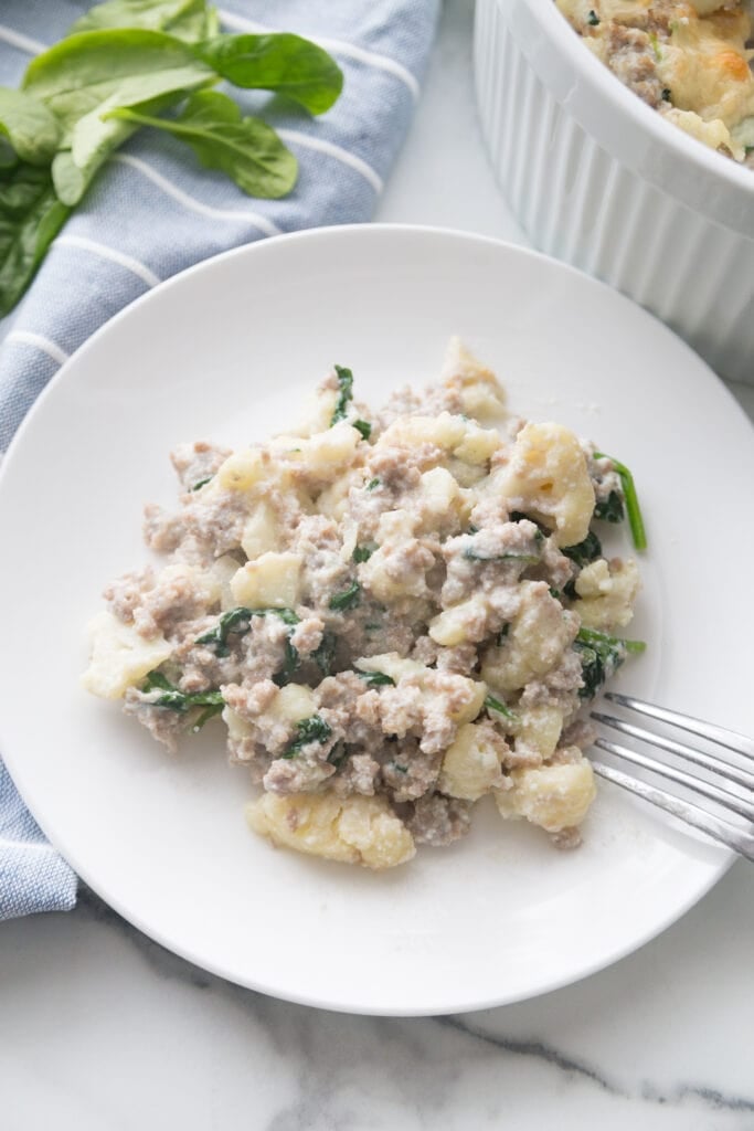 A white ceramic plate with sausage and cauliflower casserole made with ricotta and parmesean cheese 