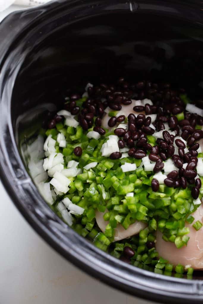 Bell peppers, onion, and black beans on top of uncooked chicken breast in a slow cooker.