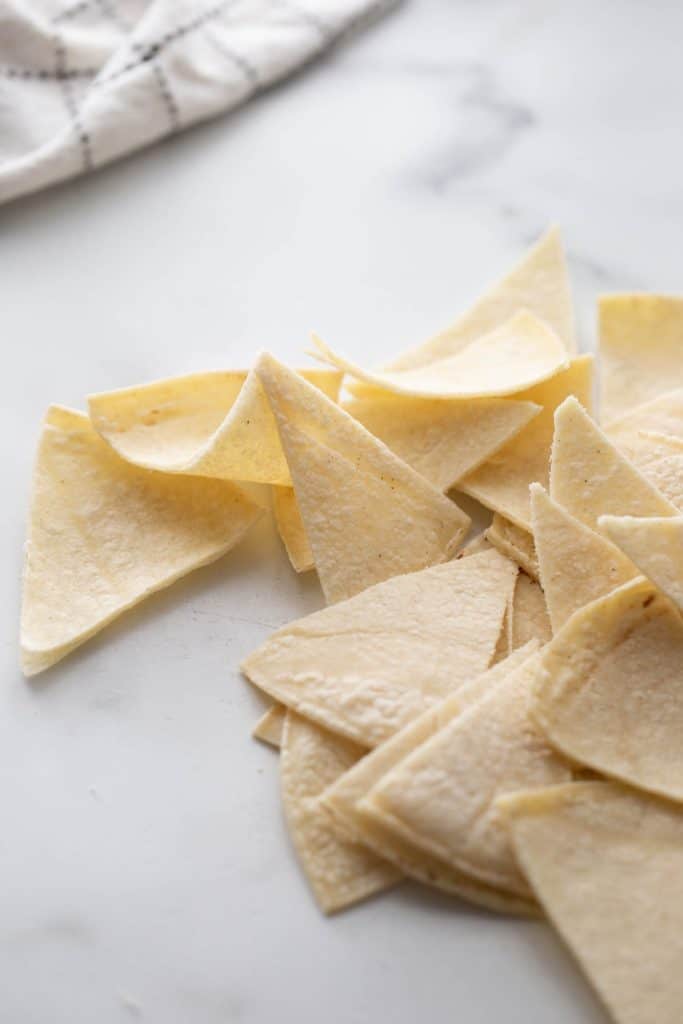 Corn tortillas cut into triangular wedges on a white marble background.