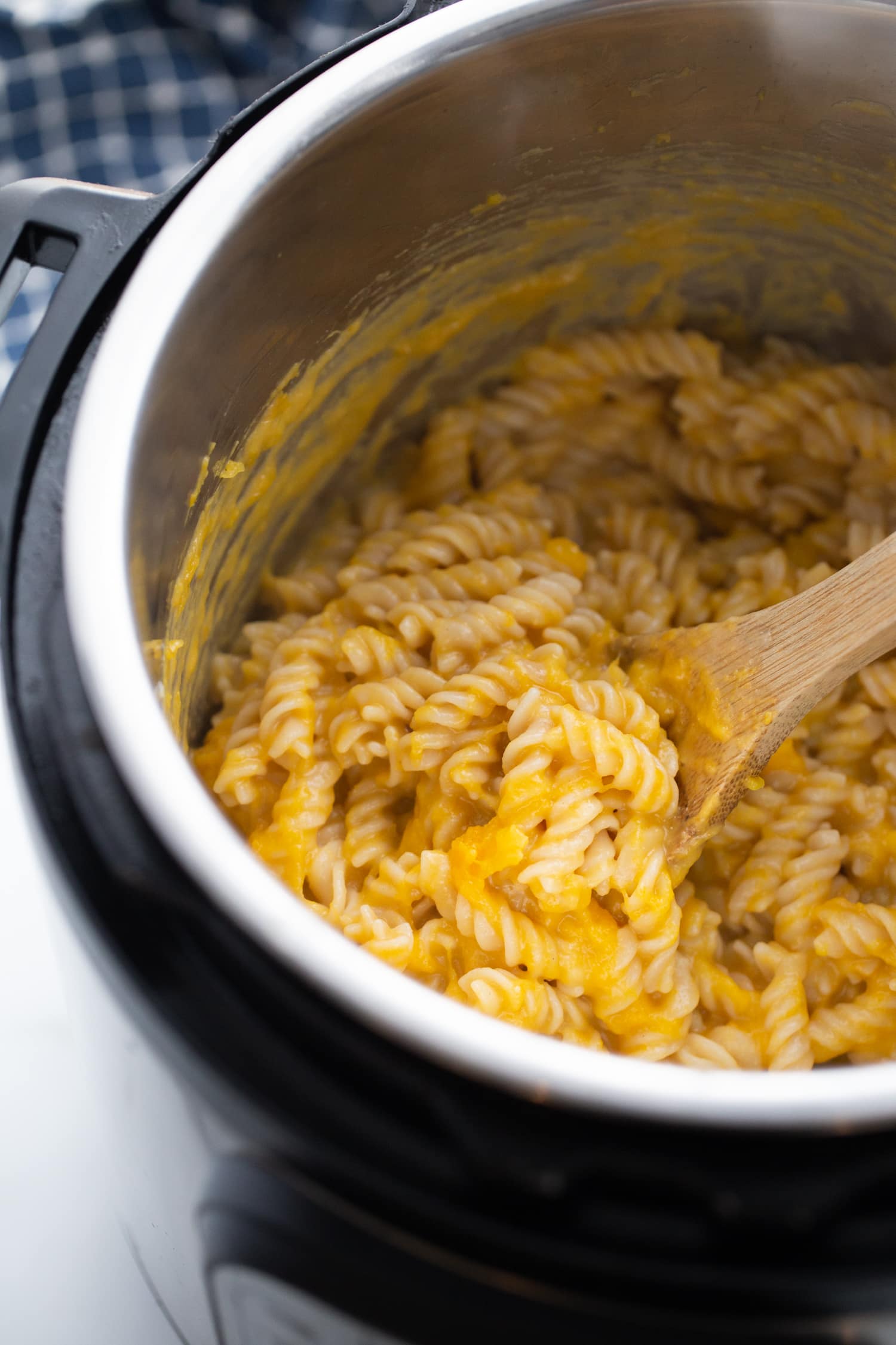 Cooked pasta in the instant pot being mixed by a wooden spoon.