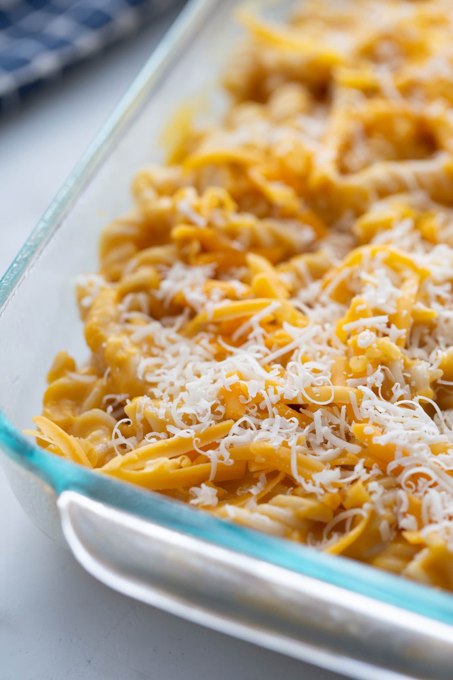 Glass baking dish of butternut squash mac and cheese topped with shredded cheese, ready for the oven.