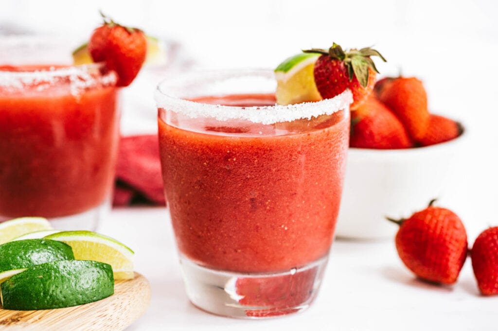 Strawberry Rhubarb Margarita garnished with lime and strawberries and a bowl of berries and some lime in the background 