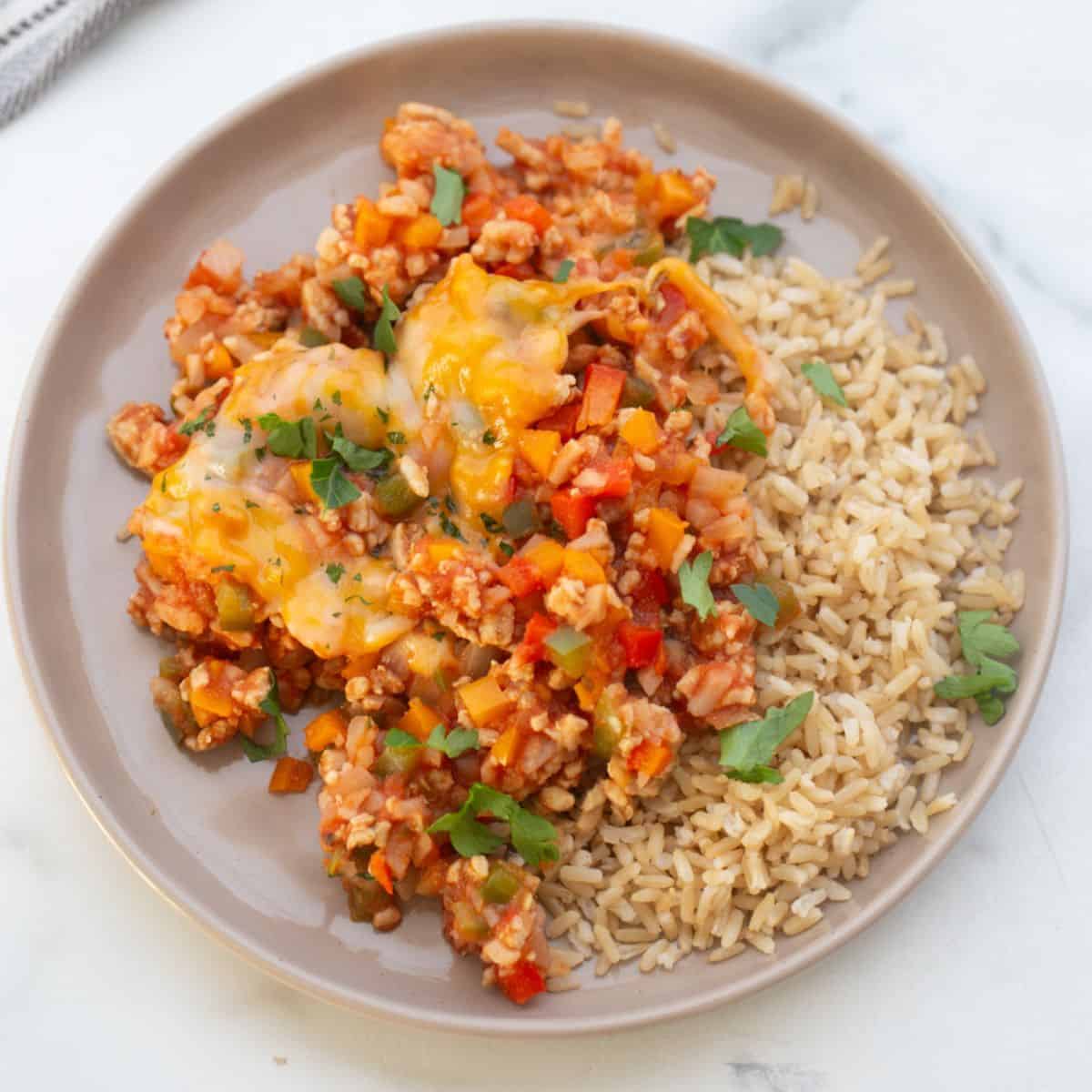 Unstuffed pepper skillet on a shite rimmed plate served with brown rice and garnished with fresh parsley.