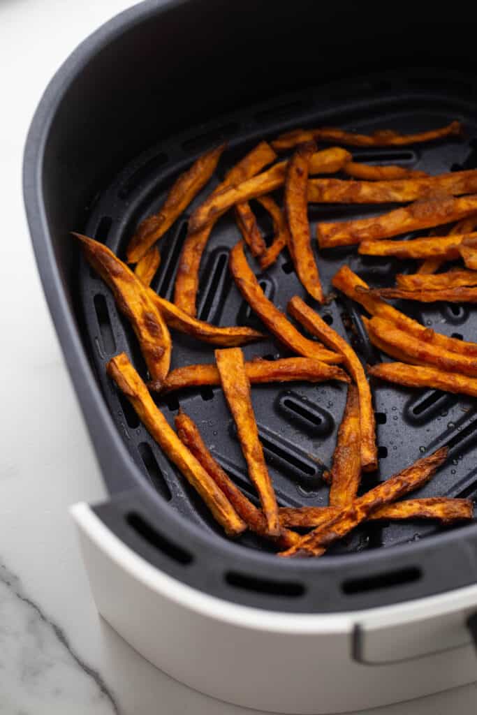 An air fryer basket with hand cut sweet potatoes.