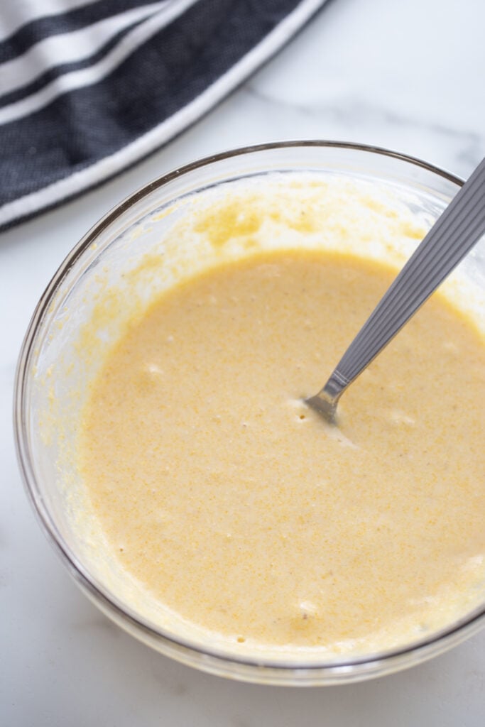 Gluten free cornbread batter in a glass bowl with a utensil.