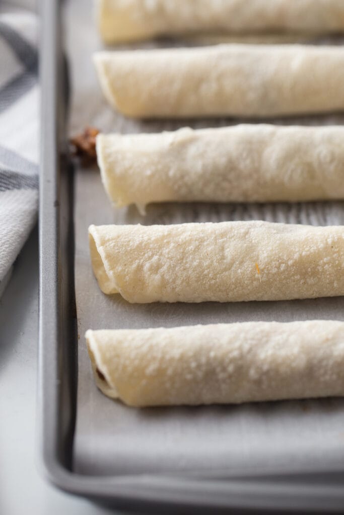 Beef taquitos lined up on a parchment lined baking sheet