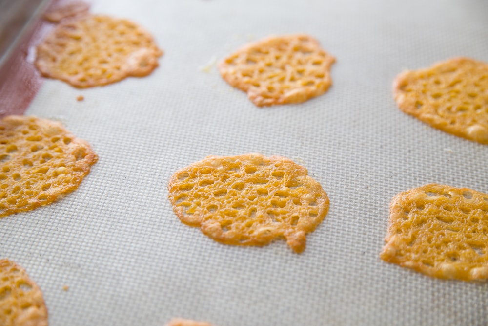 A silpat with crispy cheese chips on a baking sheet