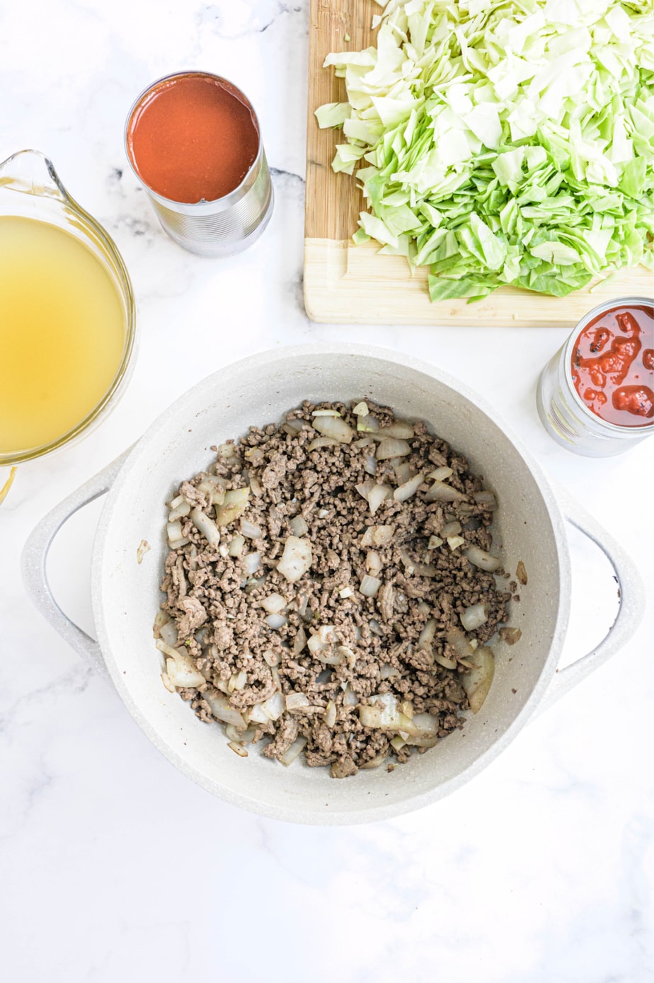 The ingredients for cabbage soup are placed on a white surface.