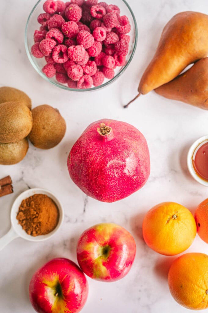 Several fruits including a pomegranate, raspberries and oranges are placed on a white marble surface.