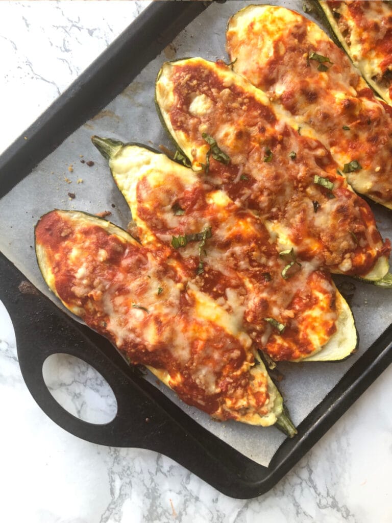 Baking sheet with Lasagna Stuffed Zucchini Boats on a marble backdrop. Boats have been broiled and the cheese is bubbly and crispy.