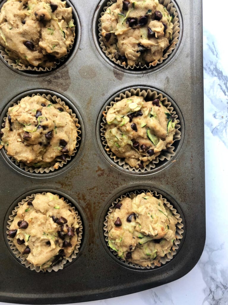 Close up photo of a partial muffin pan filled with fresh out of the oven Gluten Free Chocolate Chip Zucchini Muffins