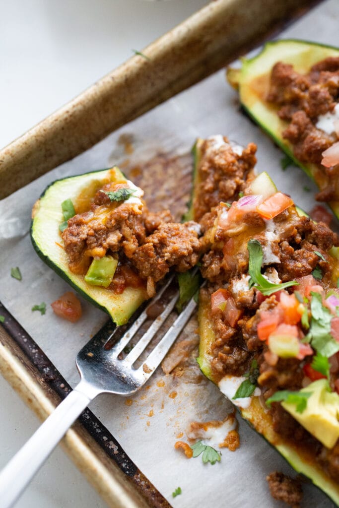 Close up photo of a fork cutting a bite of stuffed zucchini on a baking sheet.